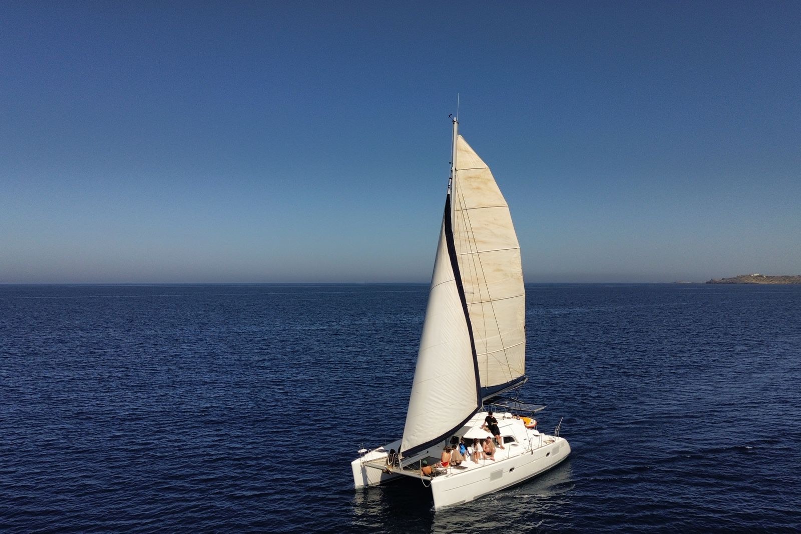 Group of people relaxing on the deck of a white sailing catamaran on open blue water