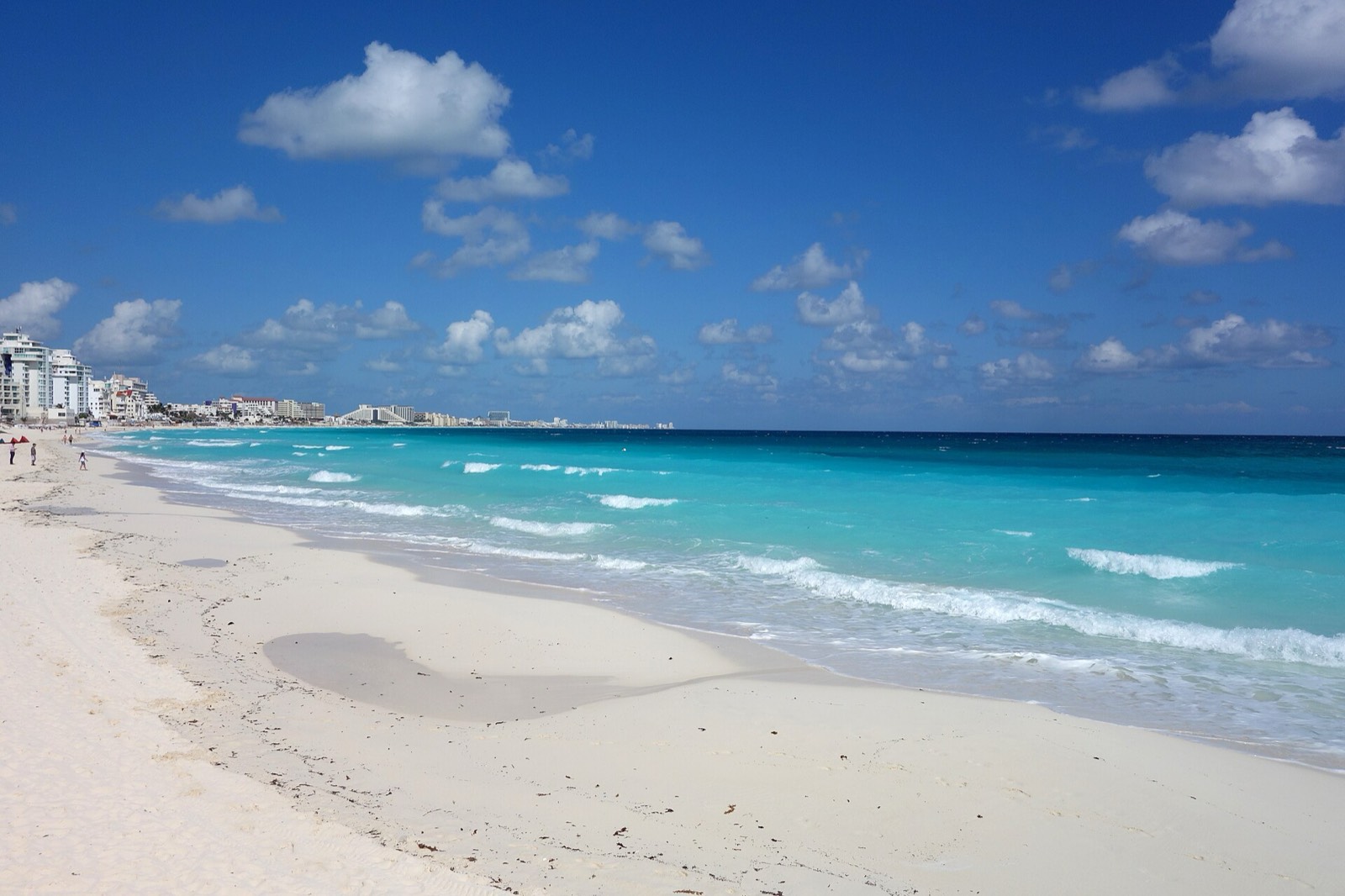 White sand beach and turquoise Caribbean water along the Cancún Hotel Zone with hotels in the distance