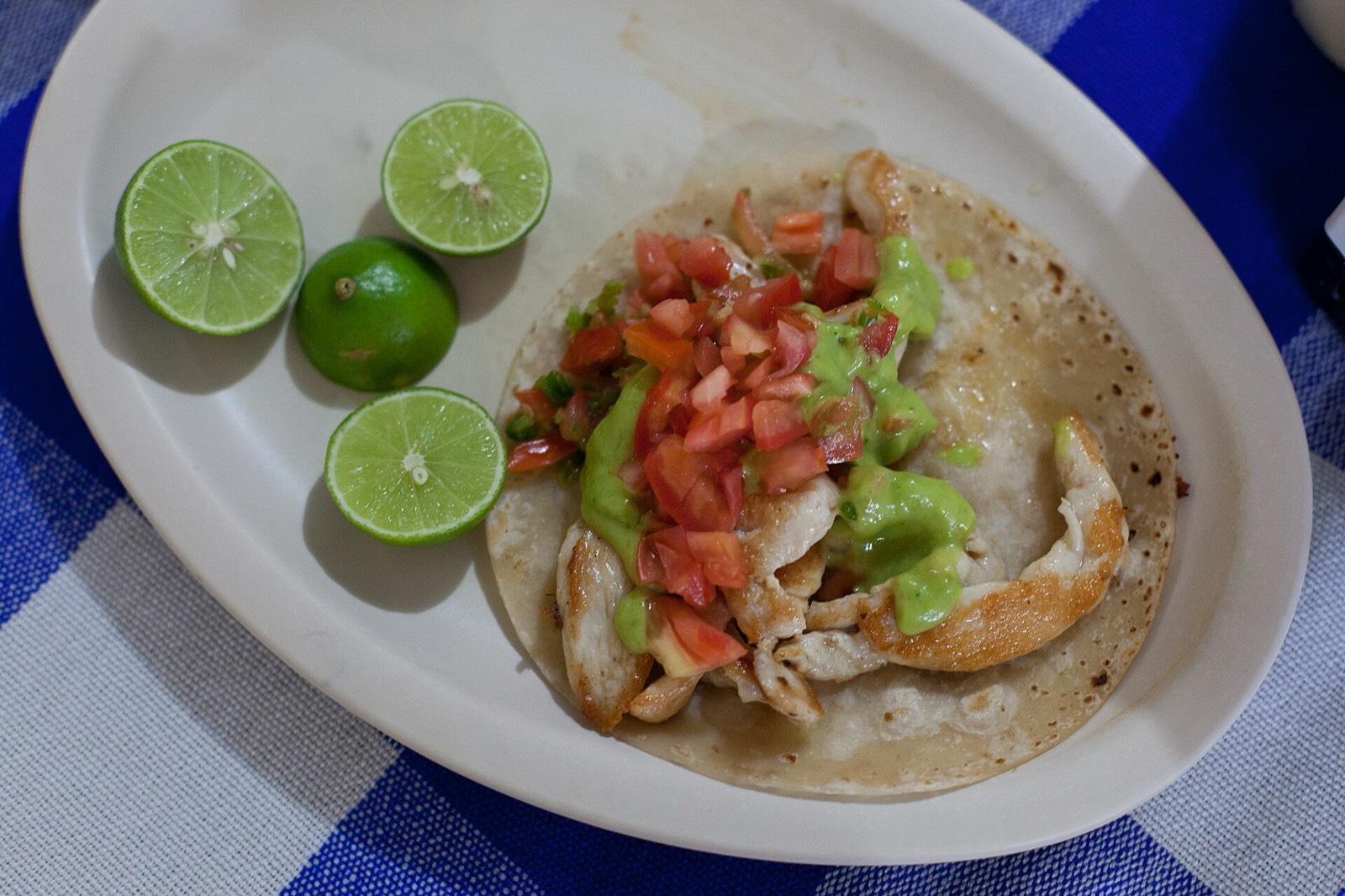 Grilled chicken taco topped with salsa and green sauce next to lime wedges on a white plate