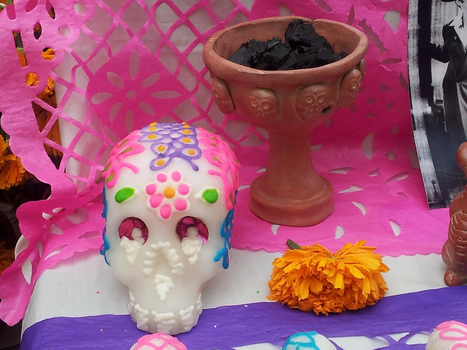 A painted sugar skull and marigold flower beside papel picado on a Día de los Muertos altar