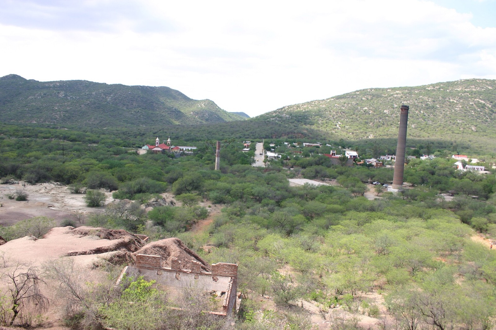 El Triunfo seen from a hillside, with an old mining smokestack, the church, and brick ruins among desert scrub