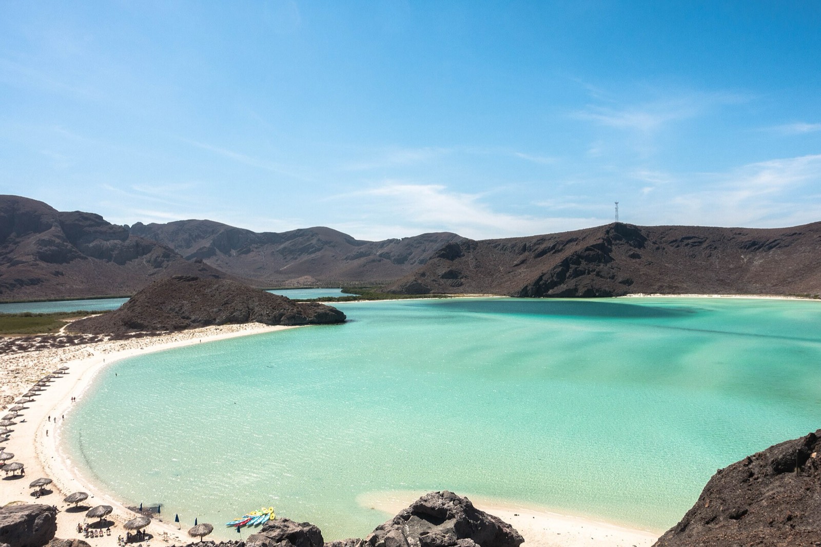 Balandra's shallow turquoise lagoon and white sand beach with palapas, ringed by desert hills near La Paz