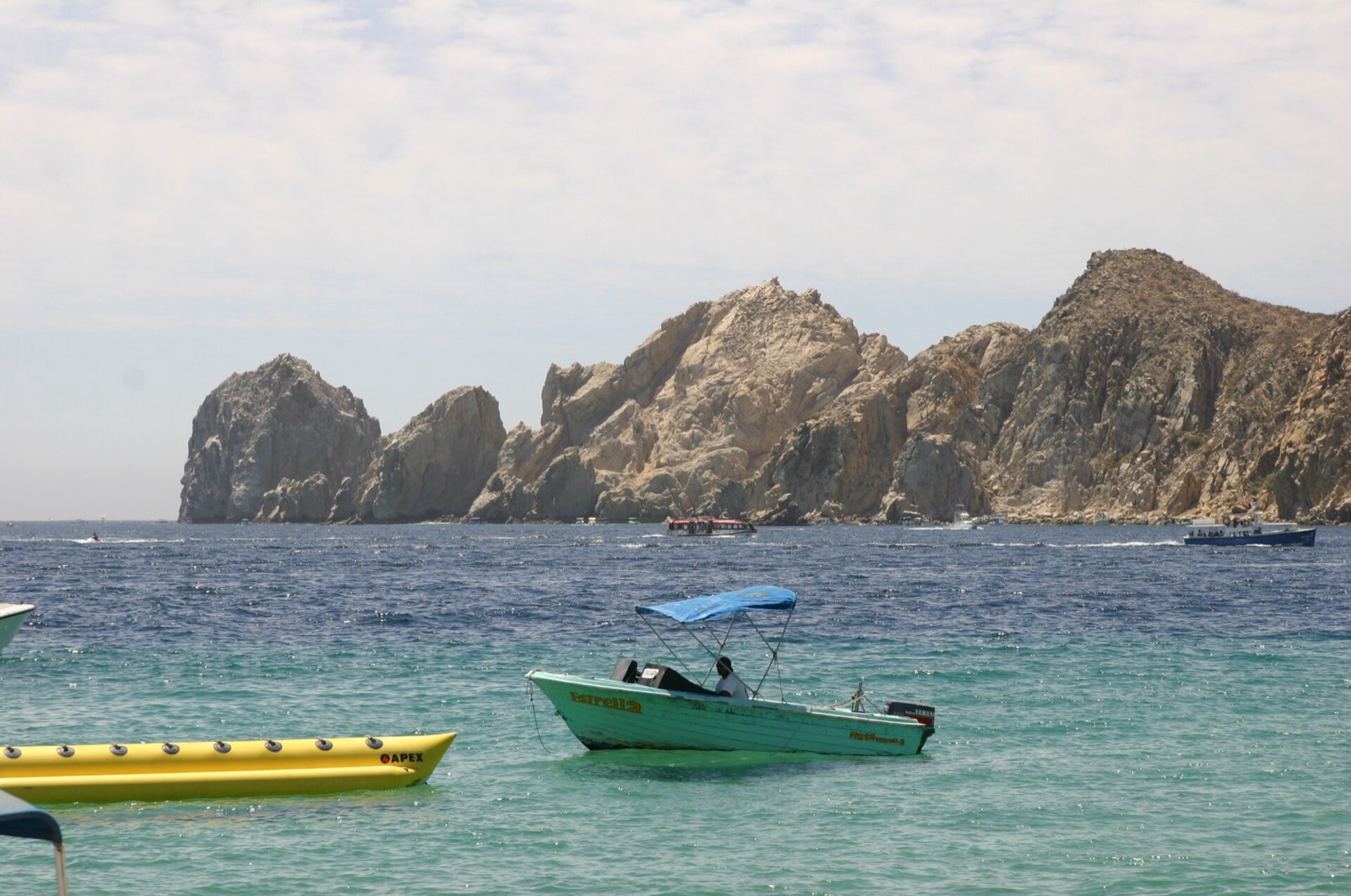 Banana boat and small boat in calm turquoise water off Médano Beach with the Land's End rocks behind