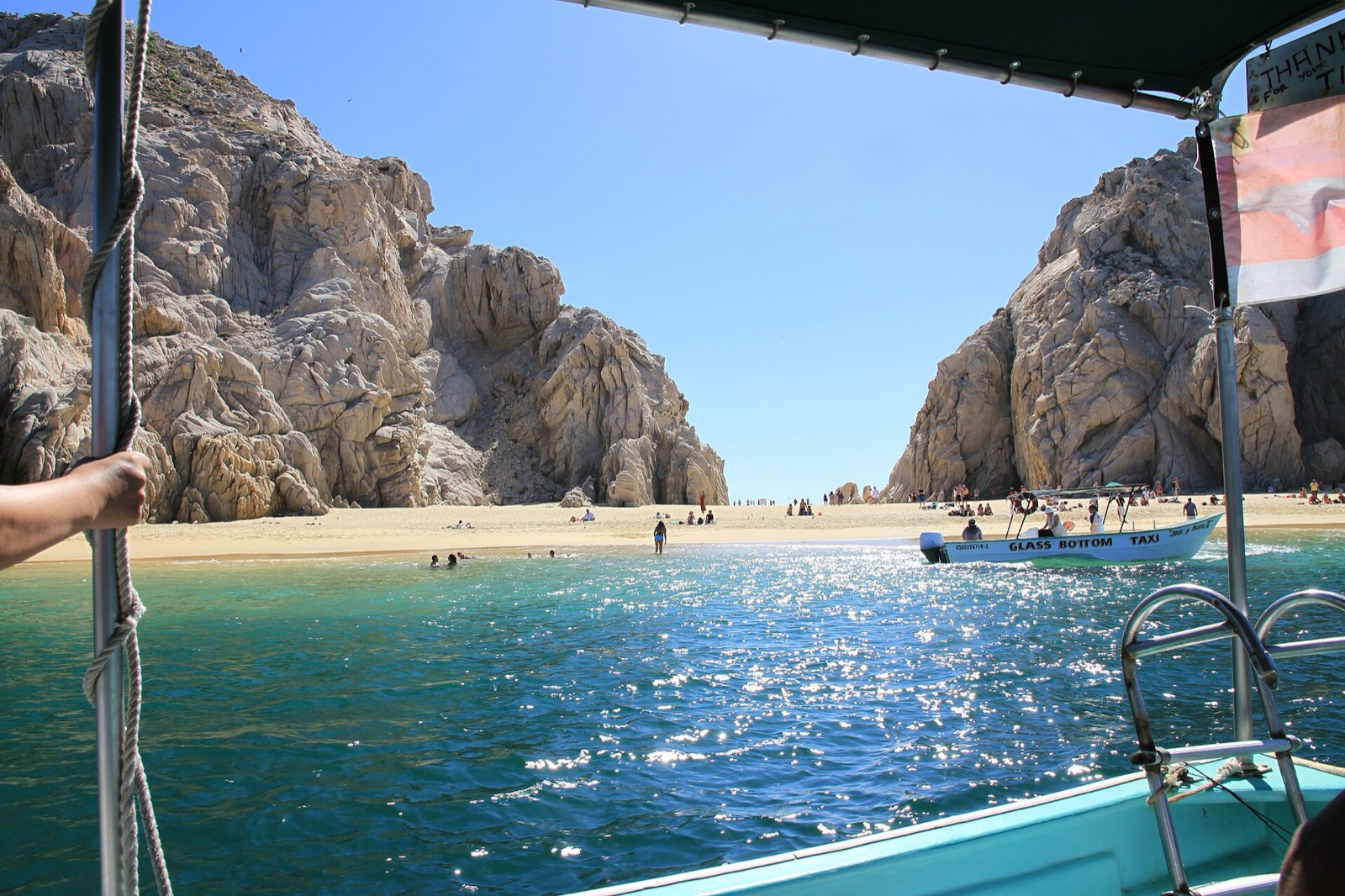 Water taxi arriving at Lover's Beach, Cabo San Lucas, with calm turquoise water between granite cliffs