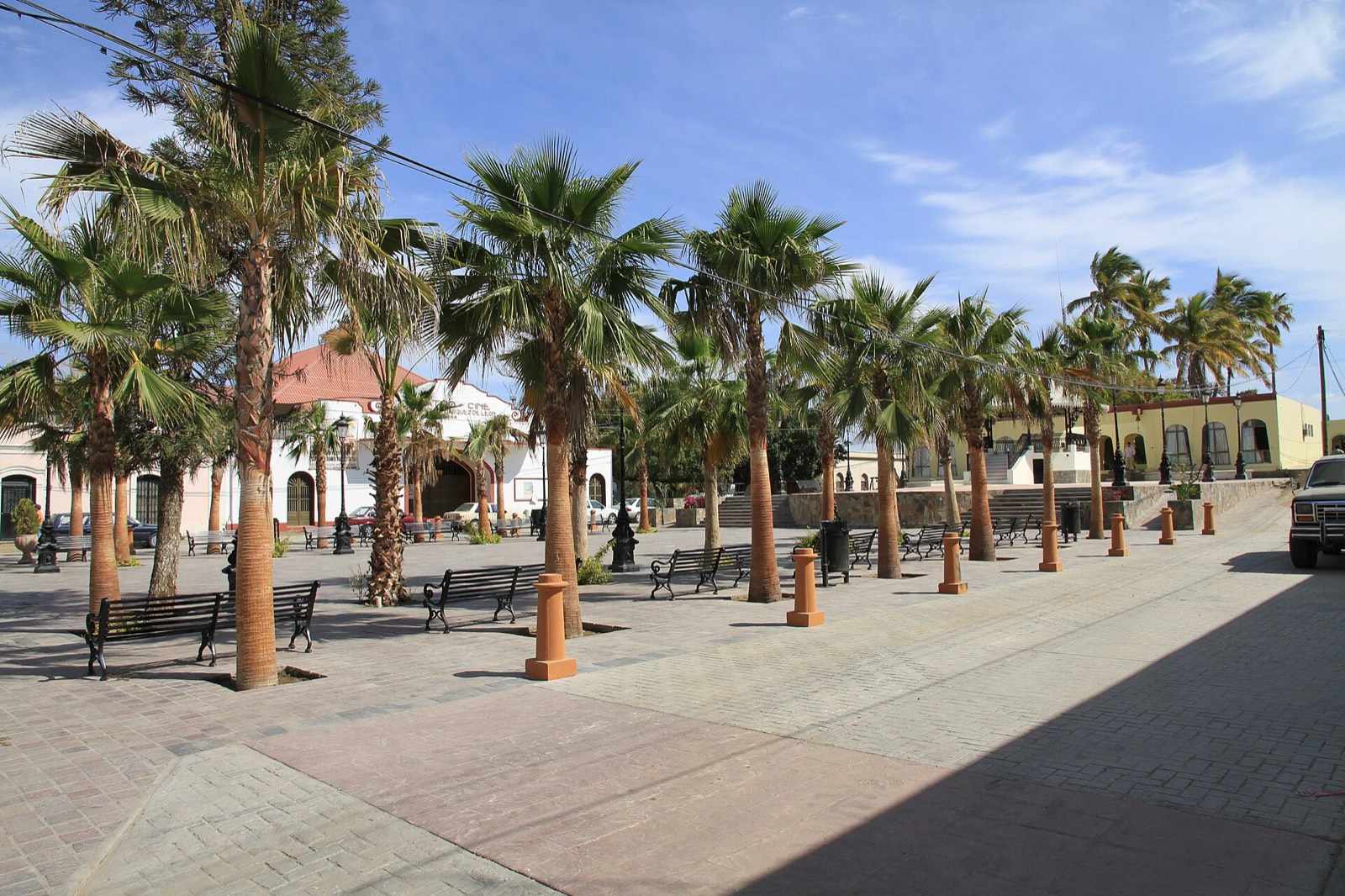The palm-shaded main plaza in Todos Santos with benches and historic buildings around it
