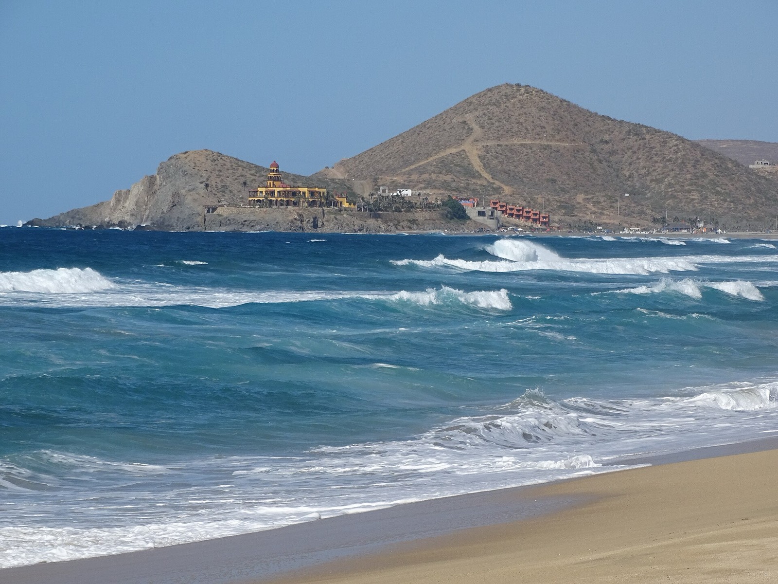 Waves rolling onto Cerritos Beach near Todos Santos, with a rocky point and desert hill behind